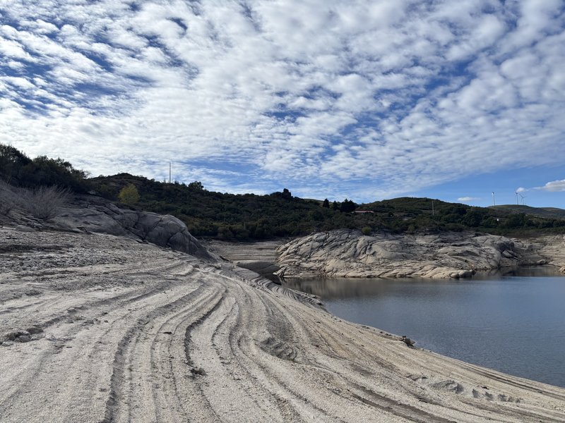 Curved bands in the exposed ground beside Alto Rabagão; granite, water and vegetation occupy different levels of the shore.
